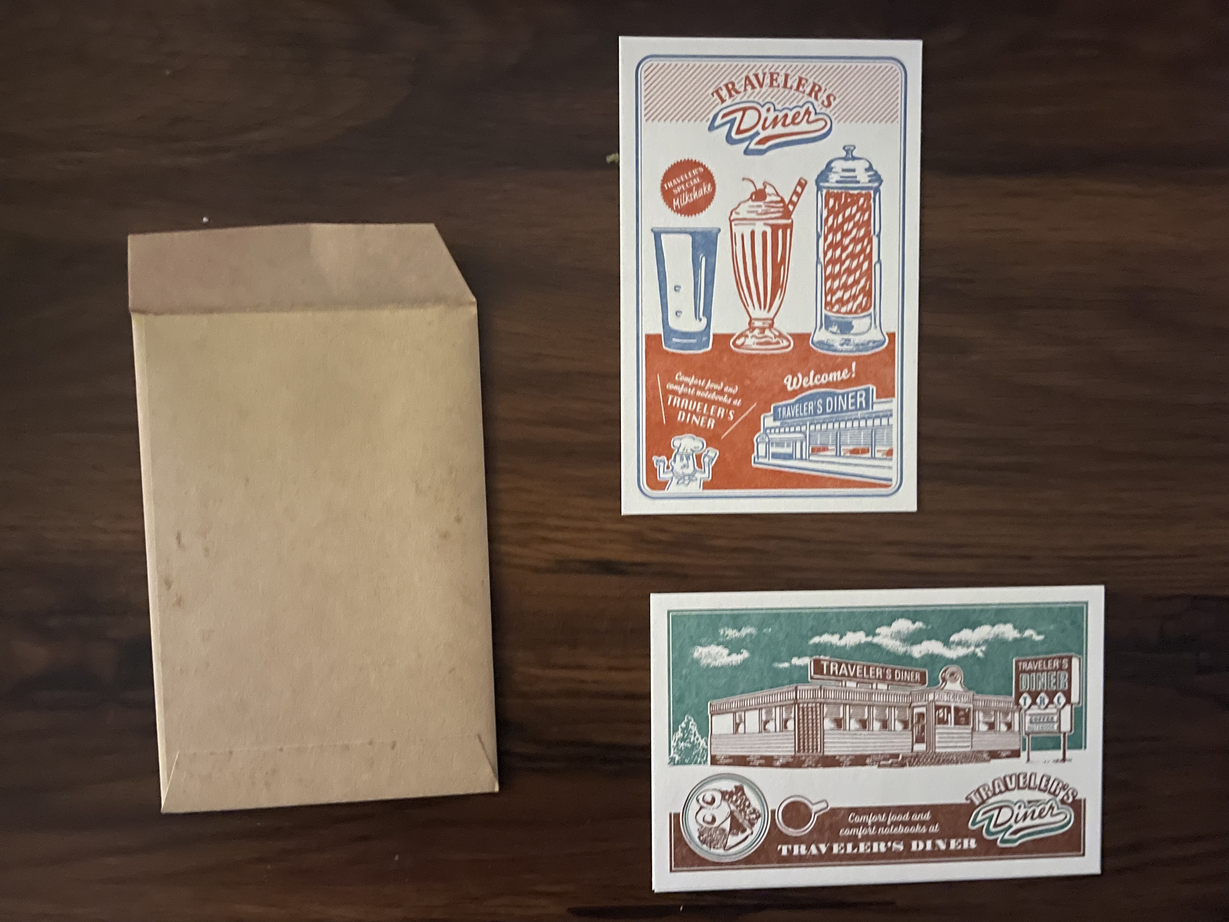 a kraft envelope and two postcards of retro diner images: one has art of a milkshake and its shaker while the other is art of a classic train car diner