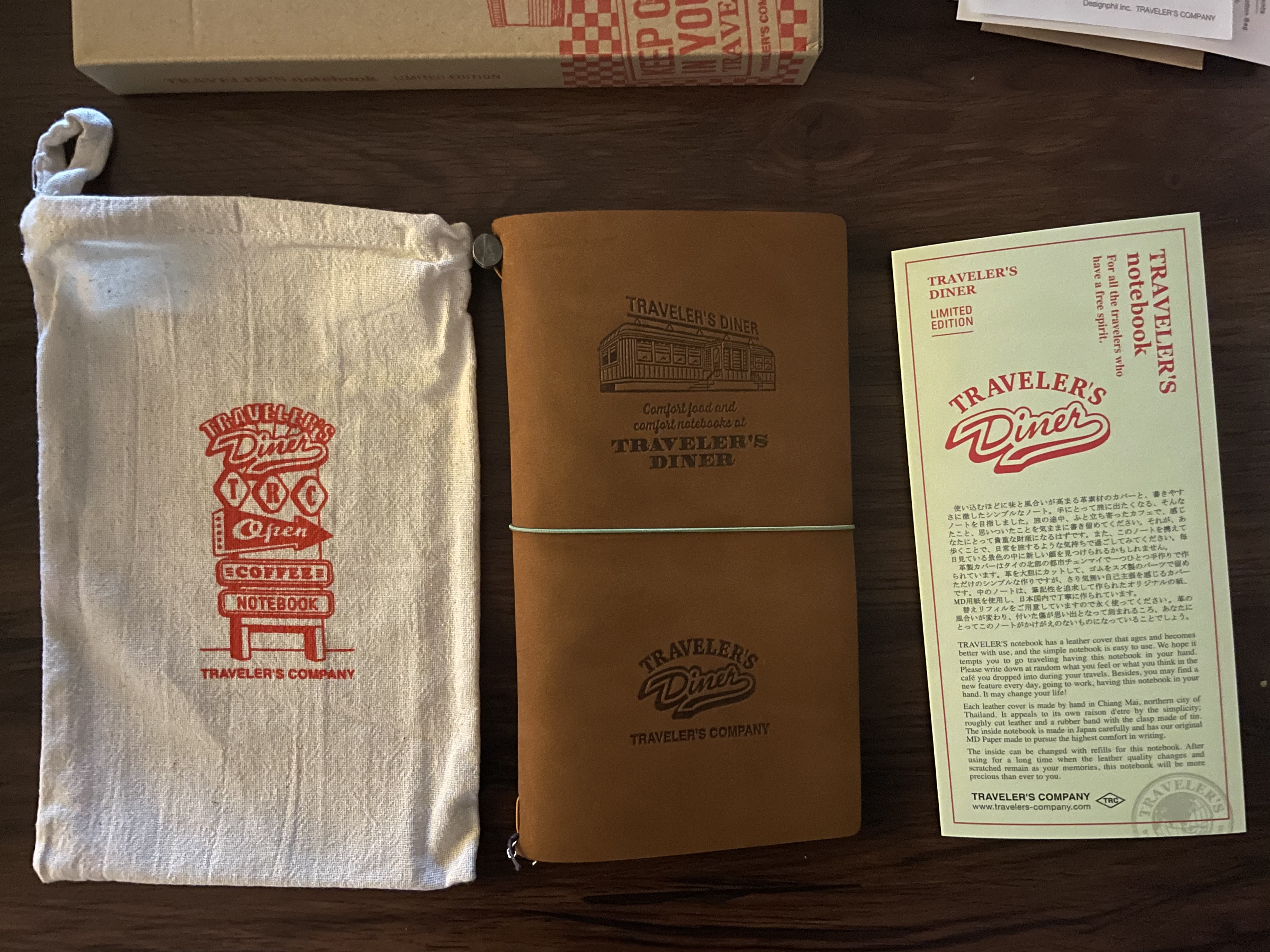 the aforementioned pamphlet next to a camel-colored traveler's notebook with the traveler's diner design on it: a train car diner with the traveler's diner logo below it