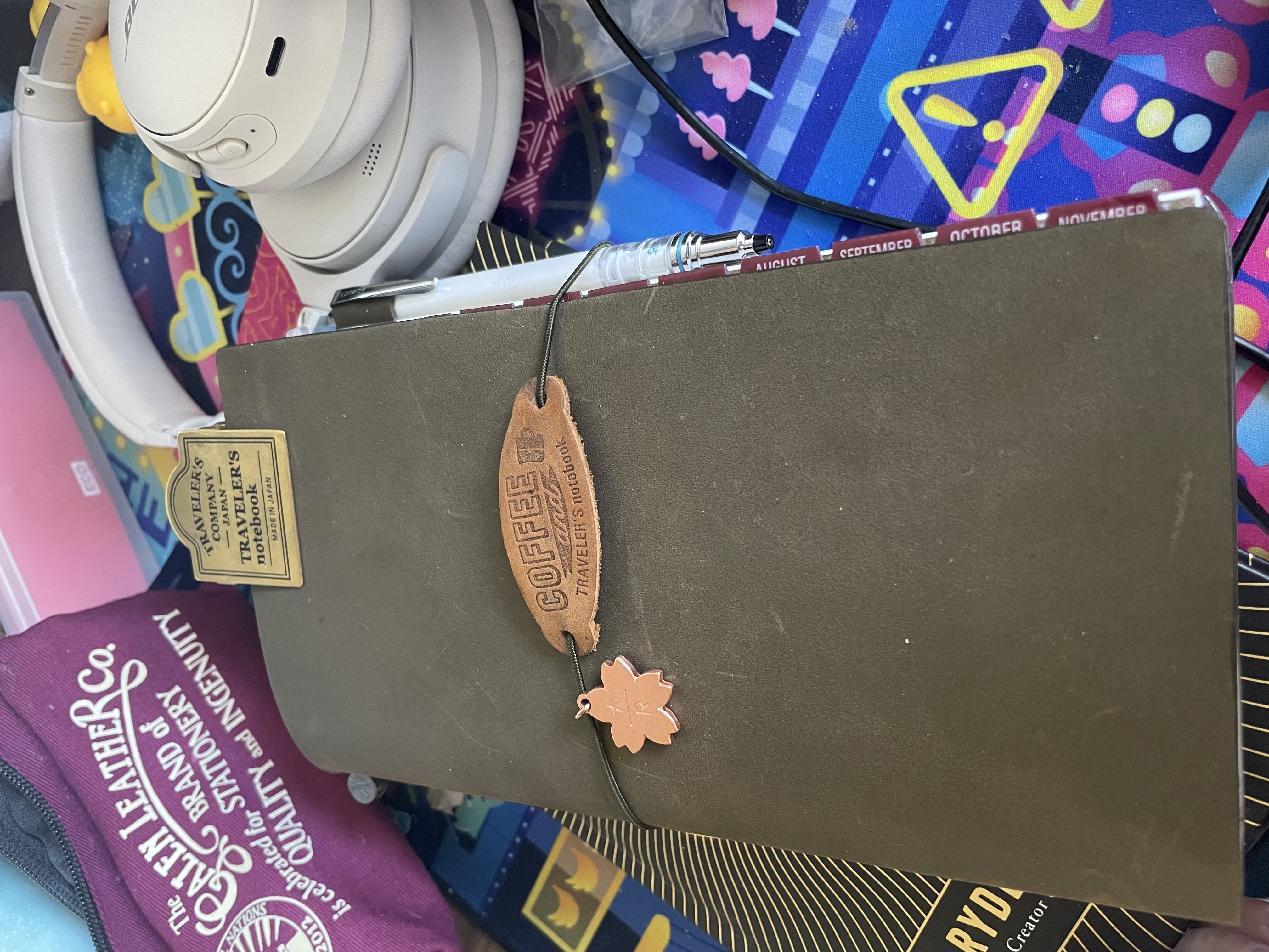 a close-up of the olive traveler's notebook fully set up with the pen holder attached: it is also adorned with a sakura flower charm and a leather tag that says 'coffee and traveler's notebook'